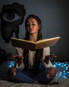 woman reading a book sitting on mattress near the blue string light inside the room